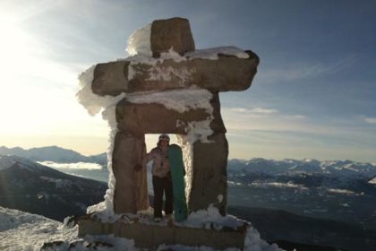 Snowboarder Karen Johanson at the top of the mountain with sun shining in the background